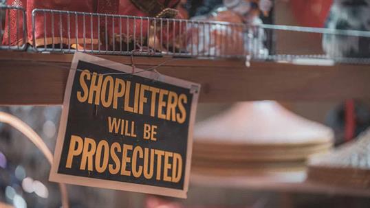 Store shelf with a posted sign warning that shoplifters will be prosecuted.